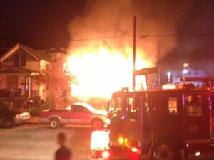 Fire department responding to a house fire, with fire engine near to camera and large flames in distance