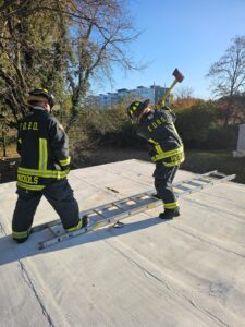 Two firefighters on the roof of a building while one is using an axe to gain access during a training exercise