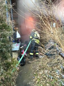Capt Jim Richmond using a hose to spray water on a fire between two houses