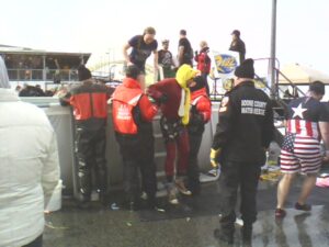 People gathered for Polar Plunge in Newport while workers help Lt./Medic Brent Schafer of BDFD out of the water while he wears a chicken hat