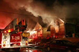 House fire with fire engine outside, smoke and flames visible