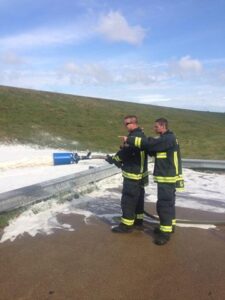 One firefighter is directed by another while spraying fire-retardant foam during training