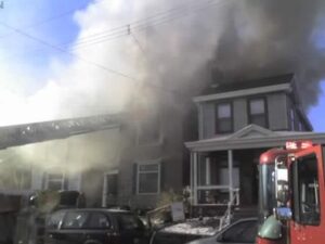 Two houses on fire with fire engine in the foreground and an engine ladder extending into the smoke