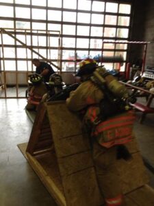 Fire department training inside with wooden props forcing firefighters to crawl and climb across the ground