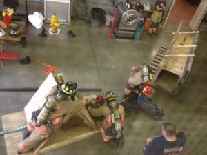 Fire department training inside with wooden props forcing firefighters to crawl and climb across the ground