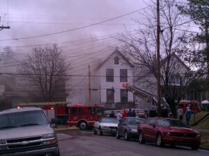 House fire in the background with smoke visible and a fire engine parked on the street