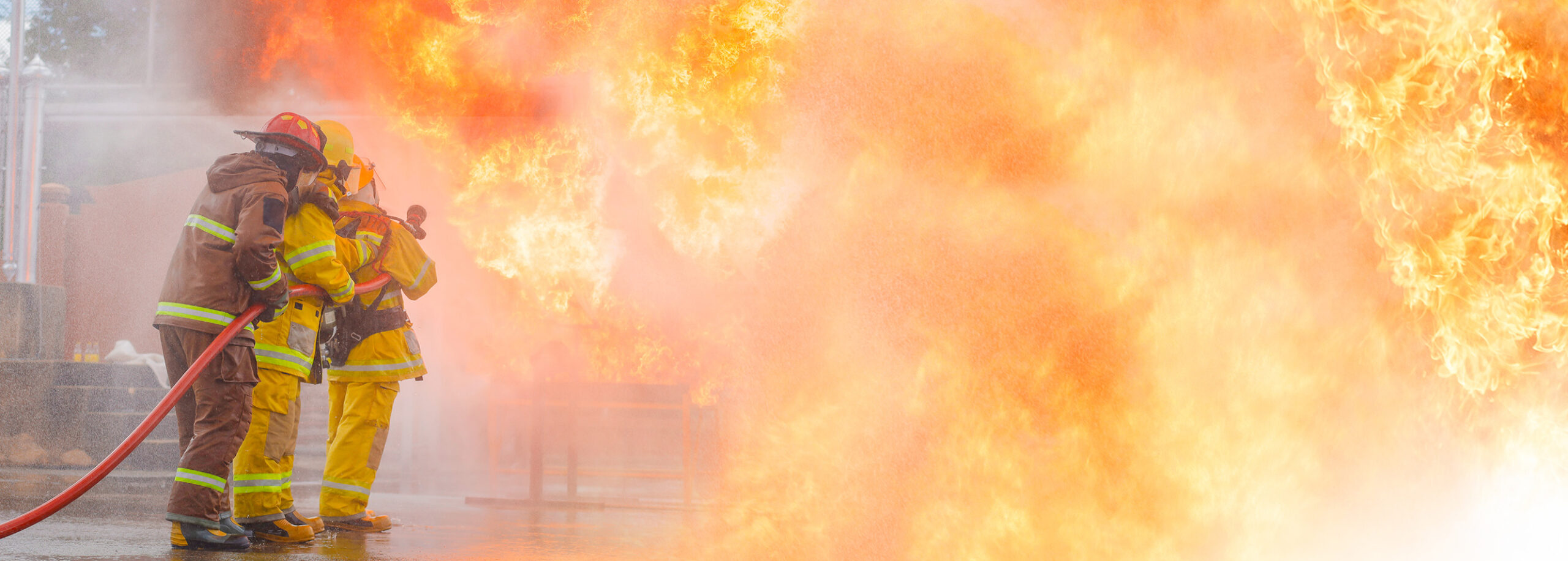 Two firefighters using a hose to spray water into a huge wall of flames